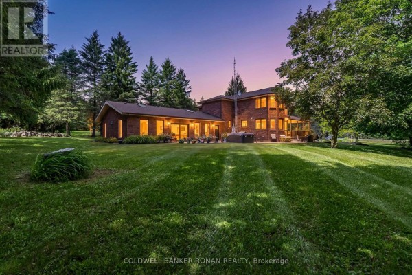 Back of the brick house at dusk with large windows glowing and trees in the background. - 1960 10th Side Road, New Tecumseth