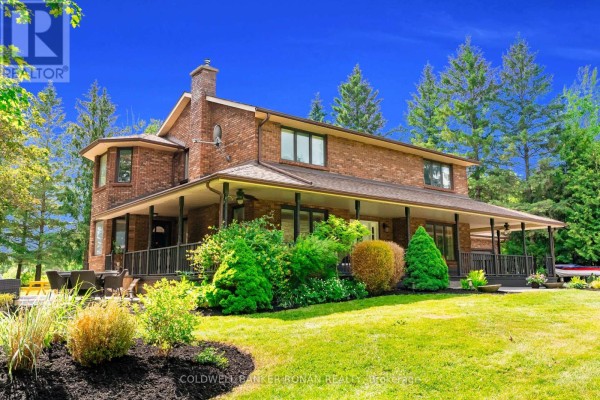 Front of the brick house with a large covered porch, mature landscaping, and mature trees. - 1960 10th Side Road, New Tecumseth