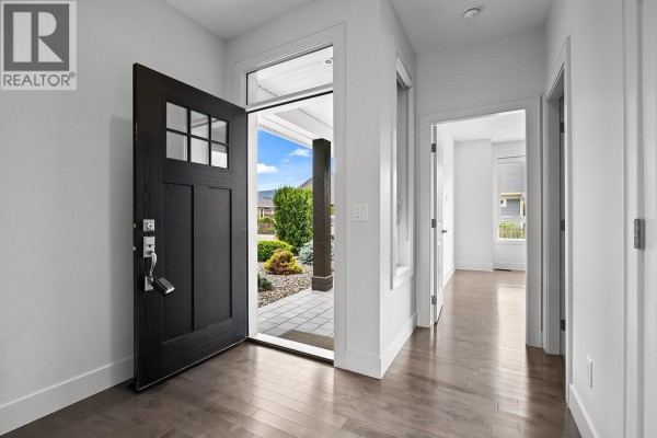 View through open front door showing entryway with dark hardwood floors and a black front door. - 1960 Klo Road Unit# 34, Kelowna