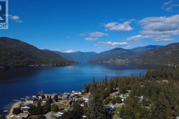 Aerial view of a small community along the shoreline of Christina Lake, with forested mountains in the distance. - 1962 Tambellini Road, Christina Lake