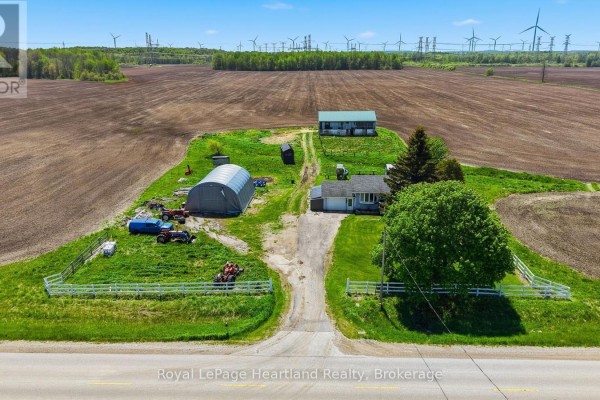 Aerial view of the farm with multiple outbuildings, fields, and distant wind turbines. - 1965 Bruce Road 20 Road, Kincardine