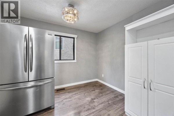 Kitchen with white cabinets, stainless steel appliances, a teal countertop, and two windows. - 1967 Harrison Way, Kamloops