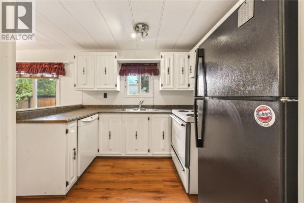 A kitchen with white cabinets, dark countertops, a black refrigerator, and wood-look flooring. - 197 Dauphin Avenue Unit# 207, Penticton