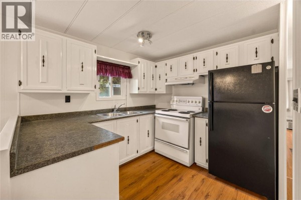 U-shaped kitchen featuring white cabinetry, dark speckled countertops, and a white stove. - 197 Dauphin Avenue Unit# 207, Penticton
