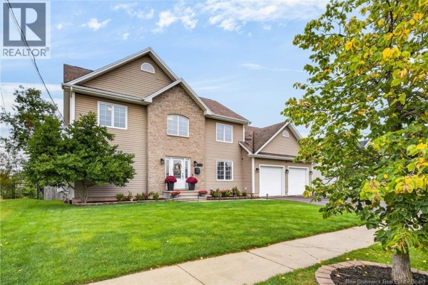 Side view of a two-story beige house with a stone facade, double garage, lawn, and walkway. - 197 Mailhot Avenue, Moncton