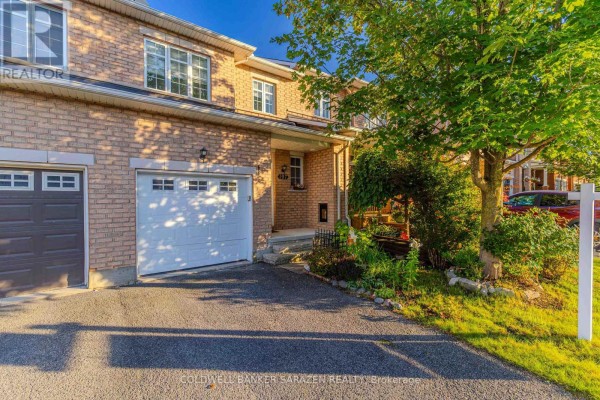 Side view of a townhouse entrance with a white garage door, brick facade, and green landscaping. - 197 Portrush Avenue, Ottawa