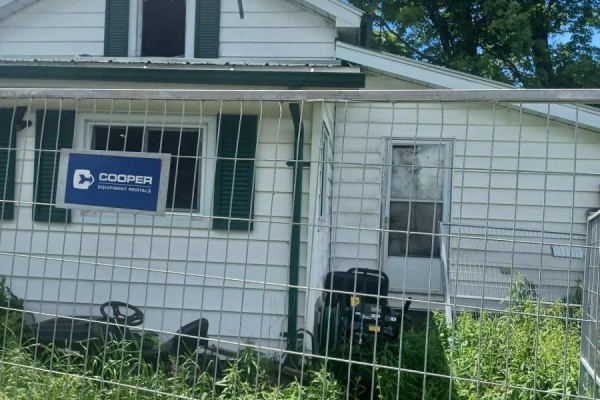 Close-up of a white vinyl-sided house with green shutters on a window, a glass-paned door, and a Cooper Equipment Rentals sign. - 1974 County Road 2 Road E, Port Hope