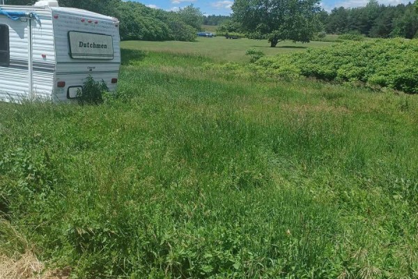 White travel trailer parked in a grassy field with trees and vegetation in the background. - 1974 County Road 2 Road E, Port Hope