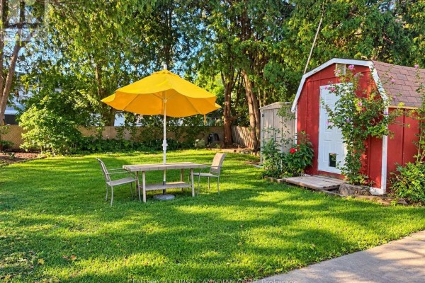 Backyard with green grass, a table set, yellow umbrella, and red shed. - 1976 Royal Crescent, London East