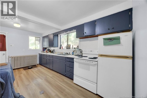 Kitchen with dark blue cabinets, white appliances, light wood laminate flooring, and a radiator. - 1979 Westfield Road, Saint John