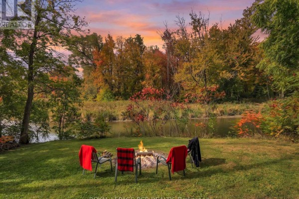 Backyard fire pit with chairs by a river surrounded by colorful autumn trees. - 19842 Yonge Street, East Gwillimbury