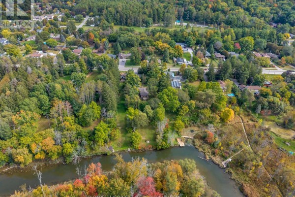 Aerial view showing the property's wooded area, riverfront, and proximity to a suburban neighborhood. - 19842 Yonge Street, East Gwillimbury