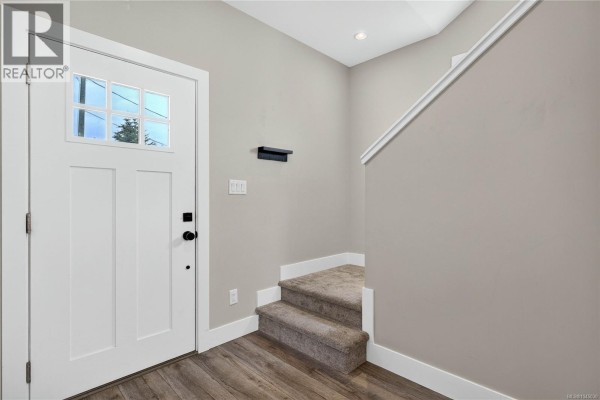 Entranceway of duplex with white door, carpeted stairs, and wood-look flooring. - 1985 Atherly Close, Sooke