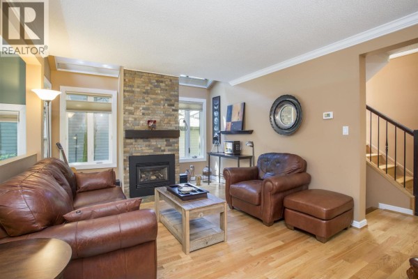 Living room with a brick fireplace, brown leather sofas, and openings to other rooms. - 1989 Cedar Village Crescent, North Vancouver