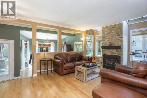 Living room with a television, leather sofa, coffee table, and openings to other rooms. - 1989 Cedar Village Crescent, North Vancouver