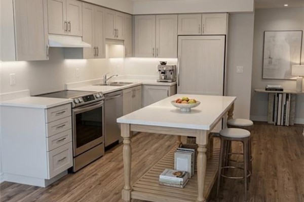 A modern kitchen with light grey cabinets, a white island, and stainless steel appliances. - 1989 Ottawa Street S Unit# 28d, Kitchener