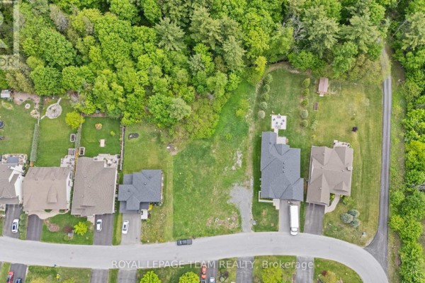 Top-down view of a grassy vacant lot with some gravel, surrounded by houses, trees, and a winding road. - 199 Charlie's Lane, Ottawa