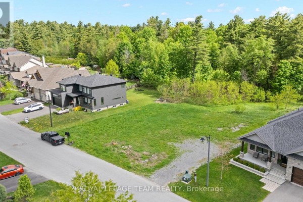 Street-level aerial perspective of an empty lot with grass and gravel, nestled between two contemporary homes. - 199 Charlie's Lane, Ottawa