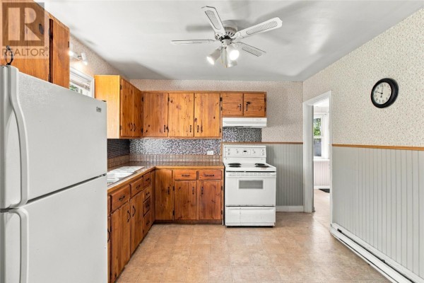 Kitchen with wooden cabinets, tiled floor, white appliances, and a door leading to another room. - 199 Freshwater Road, St  John S
