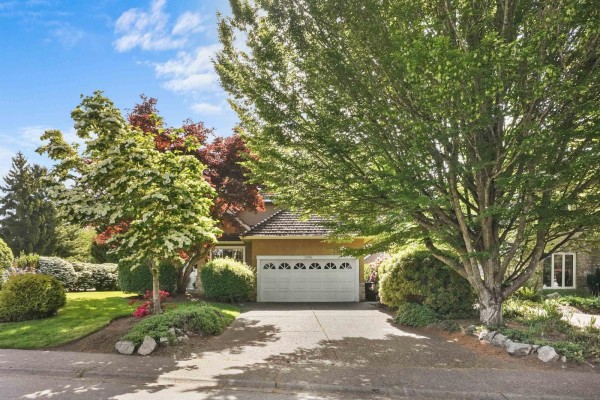 Front view of a house with a white garage door, driveway, and abundant surrounding trees. - 1990 Ocean Wind Drive, Surrey
