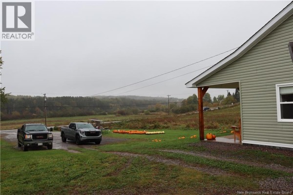A view of the property from the side, showing two trucks parked on the gravel driveway. - 1991 121 Route, Norton