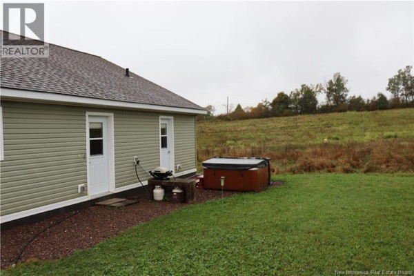 The side of the house with two doors, a grill, and a brown hot tub on the lawn. - 1991 121 Route, Norton