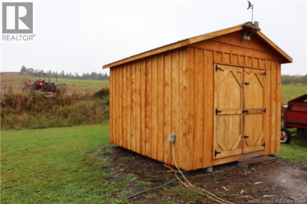 A wooden shed with double doors in a grassy field with tractors in the background. - 1991 121 Route, Norton