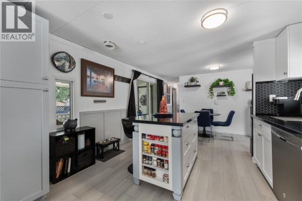 Open concept kitchen and dining area with a kitchen island, white cabinets, and gray flooring. - 1999 97 Highway S Unit# 85, West Kelowna
