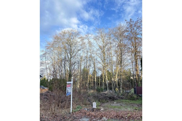Vacant lot with a for sale sign and dense trees under a cloudy sky. - 19995 50a Avenue, Langley