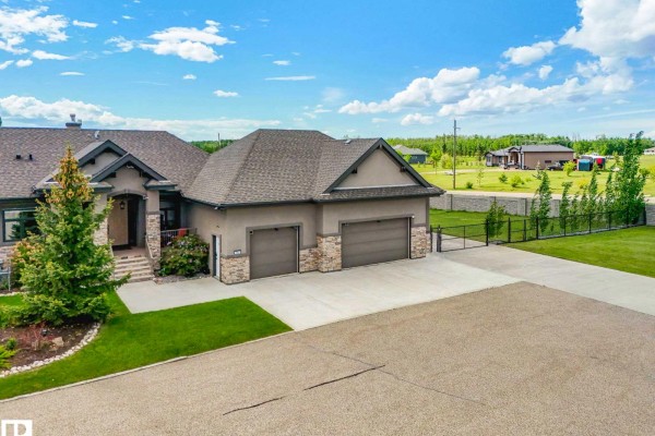 Front view of a large stucco and stone duplex with a triple garage and gated driveway. - 1a 53521 Rge Rd 272, Rural Parkland County