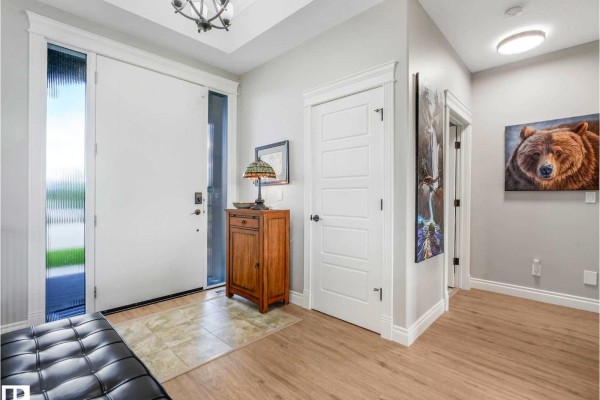 Interior entryway with a large white door, wooden cabinet, tile floor, and bear art. - 1a 53521 Rge Rd 272, Rural Parkland County