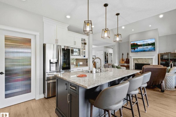 Kitchen island with granite countertop and bar stools, facing a living room with a fireplace. - 1a 53521 Rge Rd 272, Rural Parkland County