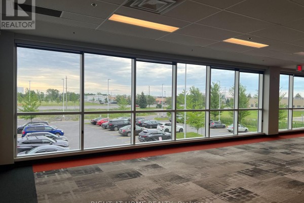 Office interior with large windows showcasing a parking lot and green trees under a cloudy sky. - 1b - 1329 Gardiners Road, Kingston