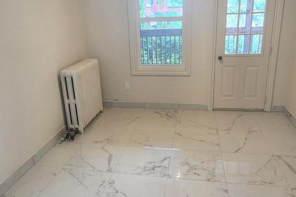 Corner of a room with white marble tile flooring, a radiator, a window, and a closed door. - 1b - 2nd Floor - 1030 St Clair Avenue, Toronto