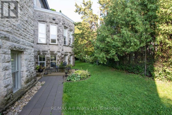 Side view of the stone building with a paved walkway, grassy yard, and mature trees. - 1c - 189 Elizabeth Street, St  Marys