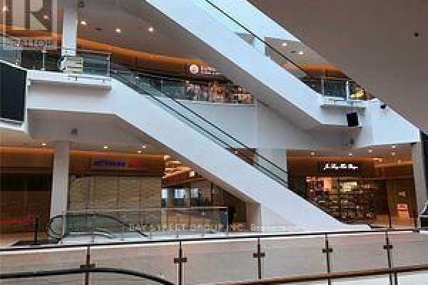 Interior view of a mall atrium with a large white staircase, escalators, and storefronts. - 1d80 - 9390 Woodbine Avenue, Markham