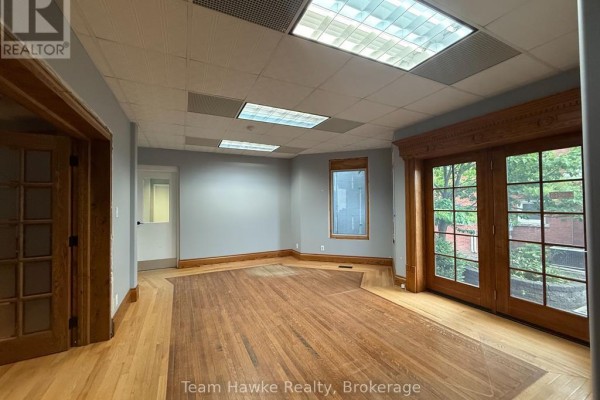 Interior office space with hardwood floors, grey walls, and double glass doors to outside. - 1e - 361 King Street, Midland