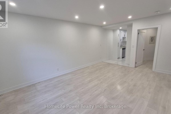 Empty living area with light wood-look flooring and white walls, leading to kitchen. - 1u - 35 Wellington Street, Brantford