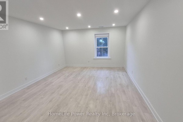 Spacious living area with light wood-look flooring and a single window facing outdoors. - 1u - 35 Wellington Street, Brantford