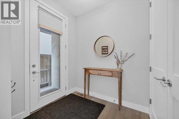Entranceway with a narrow console table, round mirror, and a glass door. - 2, 1920 25a Street Sw, Calgary