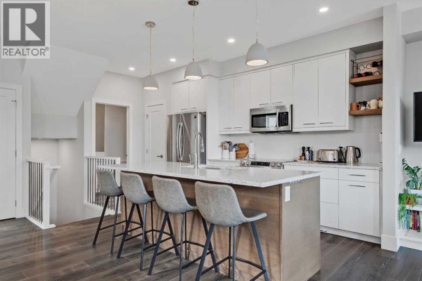 Modern kitchen with white cabinets, stainless steel appliances, and a large island with seating. - 2, 1936 25a Street Sw, Calgary