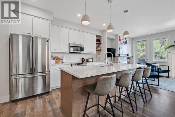 Bright kitchen and living area featuring a large island, stainless steel appliances, and dining space. - 2, 1936 25a Street Sw, Calgary