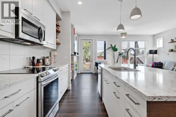 Kitchen with white cabinetry, quartz countertops, stainless steel appliances, and dark hardwood flooring. - 2, 1936 25a Street Sw, Calgary