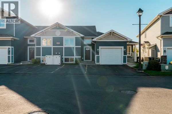Townhouse exterior featuring dark blue siding, beige trim, and a single-car garage door. - 2, 209 Lettice Perry Road N, Lethbridge