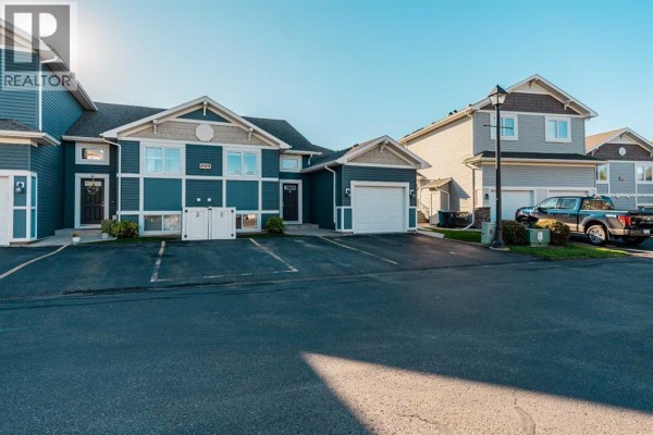 Exterior view of townhouses with dark blue and beige siding, parked cars, and asphalt driveway. - 2, 209 Lettice Perry Road N, Lethbridge
