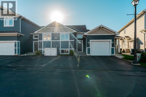 Townhouse complex exterior under bright sunlight with dark blue and beige siding and garages. - 2, 209 Lettice Perry Road N, Lethbridge