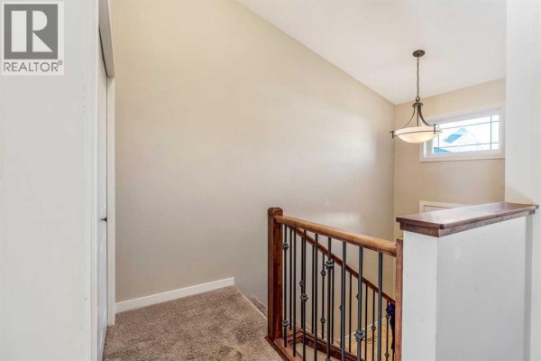 Interior staircase with beige carpet, wood railing, dark metal spindles, and a pendant light. - 2, 209 Lettice Perry Road N, Lethbridge