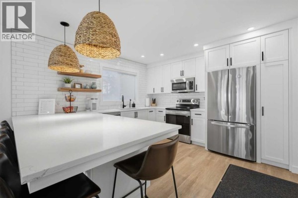 White kitchen with large island, pendant lights, stainless steel refrigerator, and subway tile backsplash. - #2, 4415 Lakeshore Drive, Sylvan Lake