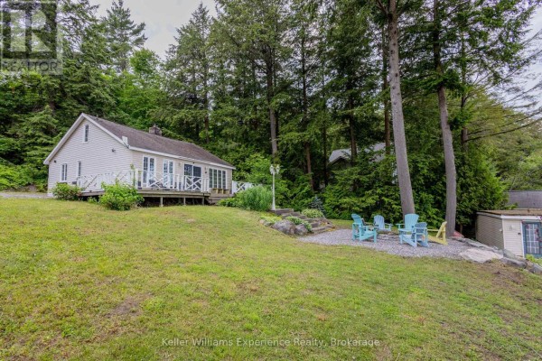 Side view of a cottage with a wooden deck and a fire pit area. - 2 - 1018 Georgina Way, Gravenhurst)