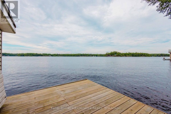 Wooden dock on a lake with a tree-lined horizon under a cloudy sky. - 2 - 1018 Georgina Way, Gravenhurst)